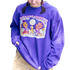 A Bizarre Coffee purple crewneck sweater with a campfire design featuring two flowers roasting marshmallows and sipping coffee.