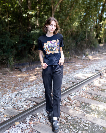 A person wearing a t-shirt with a custom design featuring a witch on a broom holding a coffee cup.